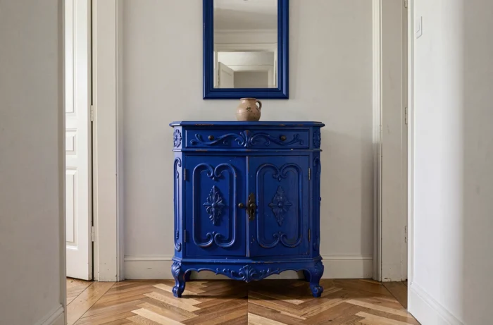 Couloir étroit avec une ancienne commode sculptée peinte en bleu cobalt intense, miroir mural au-dessus et parquet en point de Hongrie