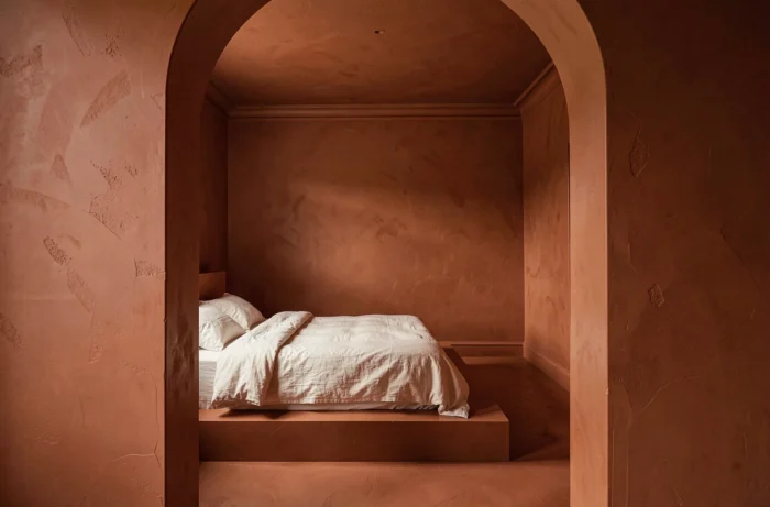 Chambre en drenching avec une seule couleur terracotta du sol au plafond et aux boiseries, lit bas avec linge de lit blanc comme seul contraste